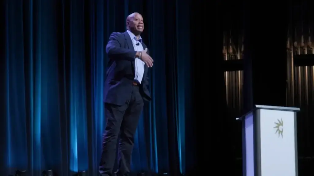 Walter Bond delivering a keynote on stage at Gaylord Palms in Orlando, in front of a teal curtain backdrop