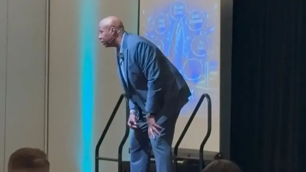 Walter Bond bent forward in laughter on stage while speaking to a seated audience