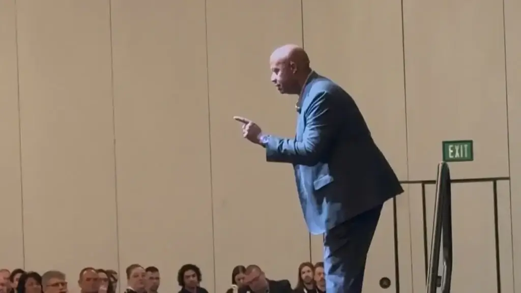 Walter Bond pointing toward the audience while speaking on stage at a corporate event